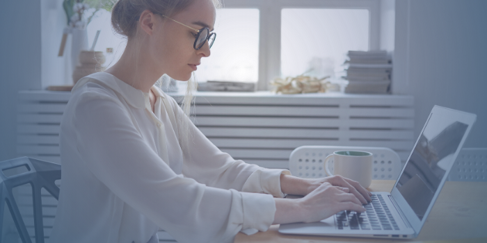 A woman sits at a desk at home, typing a resignation letter on a laptop computer