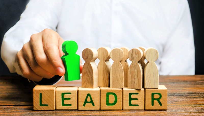 A person arranges wooden figurines, with a green figurine at the head of the colorless ones, indicating that green energy will lead the workforce of the future.